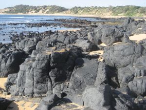 Cat Bay at Summerland with basalt boulders in foreground and sand dunes rising alongside beach in background.